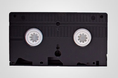 Schwarze VHS-Kassette vor einfarbigem Hintergrund mit zentrierten Spulen.