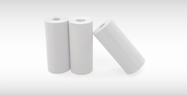 Drei weiße Papierrollen, stehend angeordnet, eine davon kippt auf einer ebenen Unterfläche.