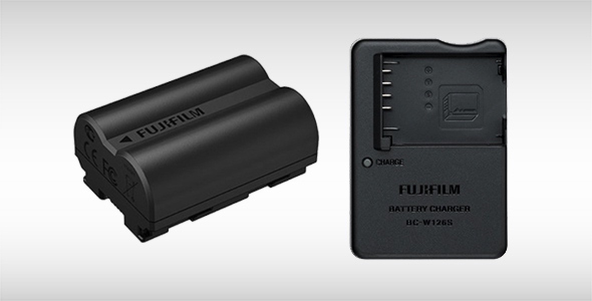 Fujifilm-Akkupack neben passendem Batterieladegerät auf neutralem Hintergrund.